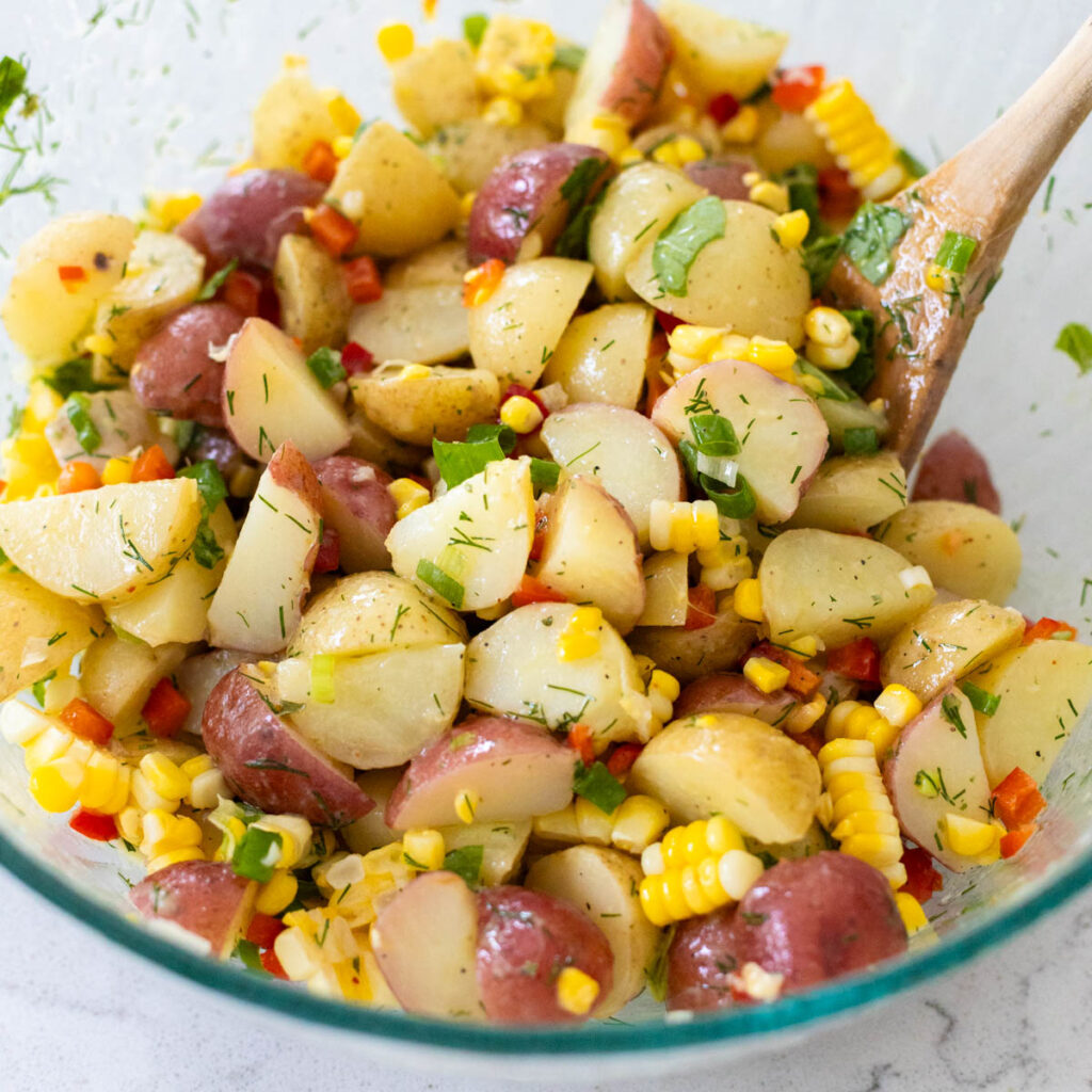 A white dish filled with potato salad mixed with corn and red bell peppers.