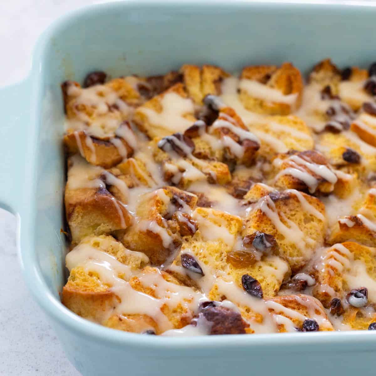 A blue baking dish is filled with a cinnamon roll casserole that has an icing drizzle over the top.