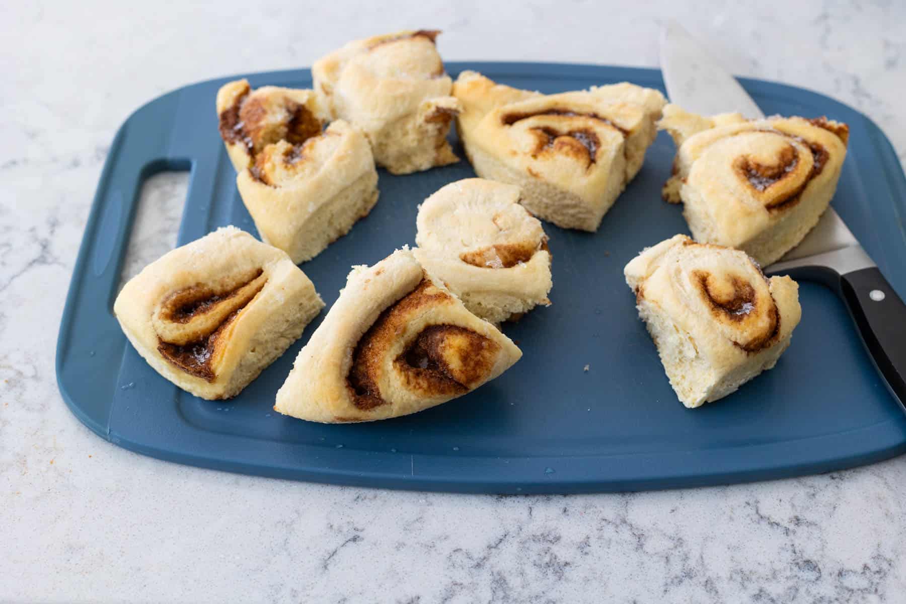 The cinnamon rolls are on a cutting board ready to be chopped.