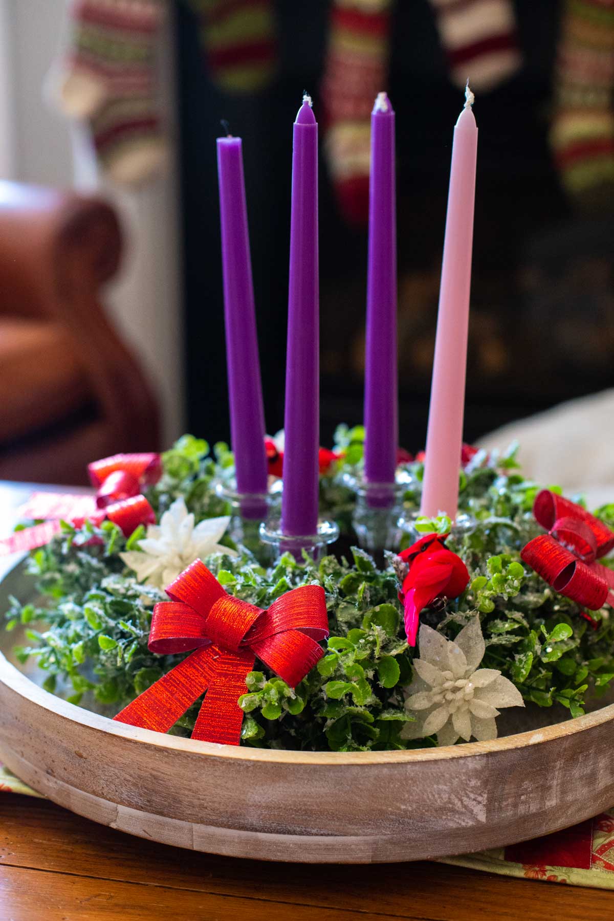 A homemade Advent wreath with purple and pink candles sits on a coffee table during the day.