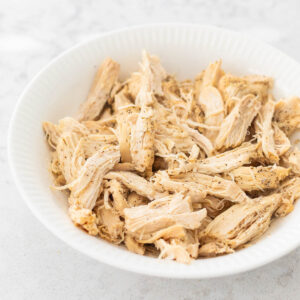 The white bowl of shredded chicken meat.