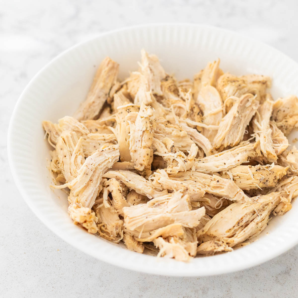 The white bowl of shredded chicken meat.