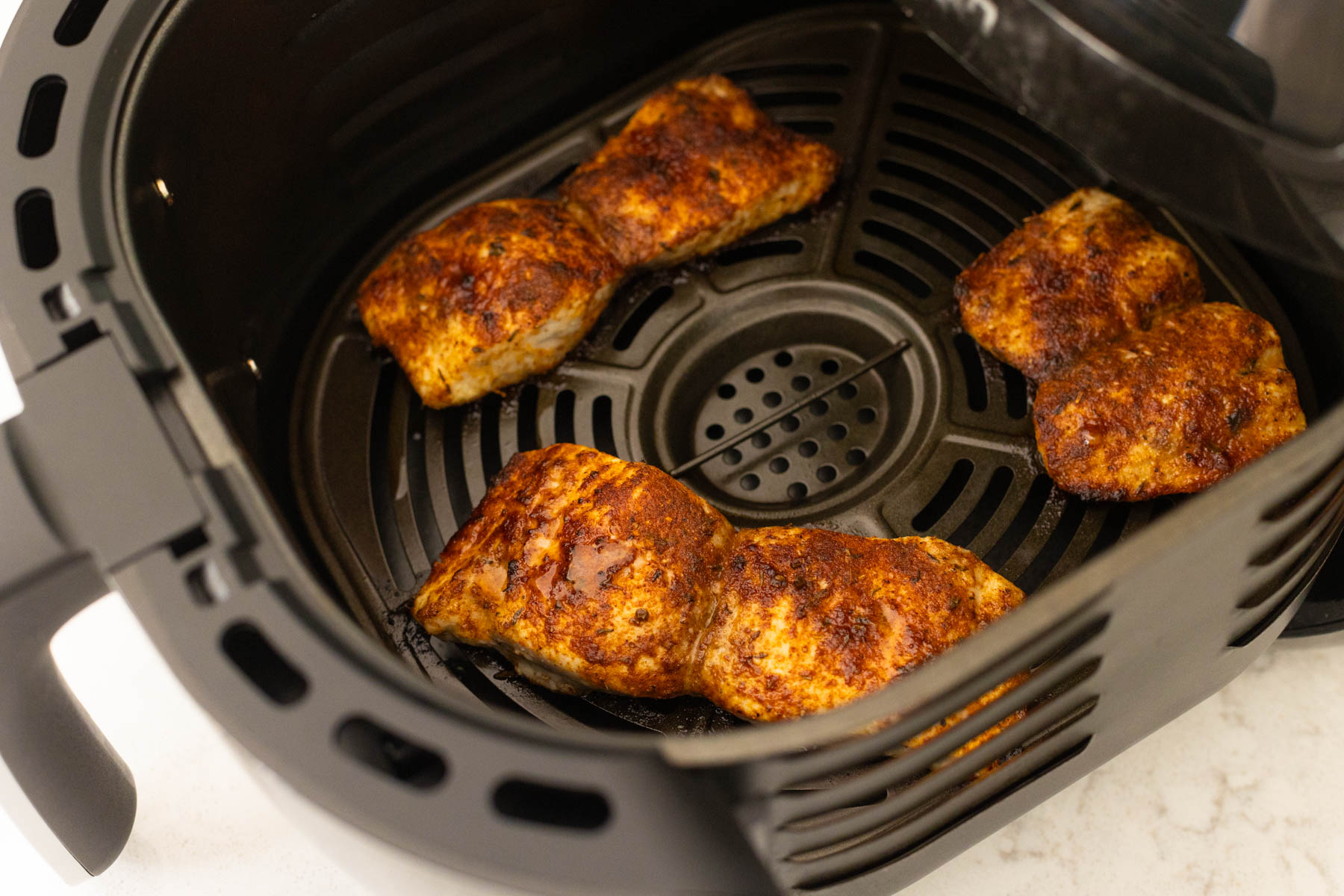 The fish filets are cooking inside an air fryer basket.
