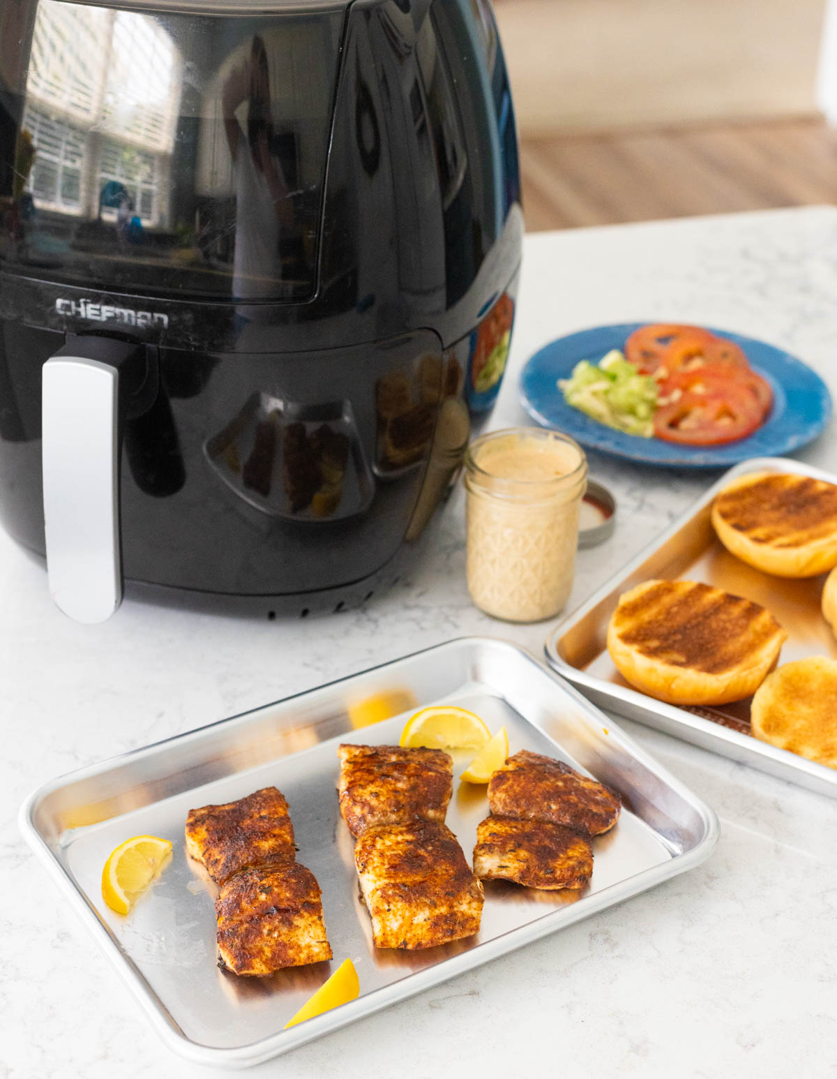 The cooked fish, buns, and sandwich toppings are on display in front of the air fryer.