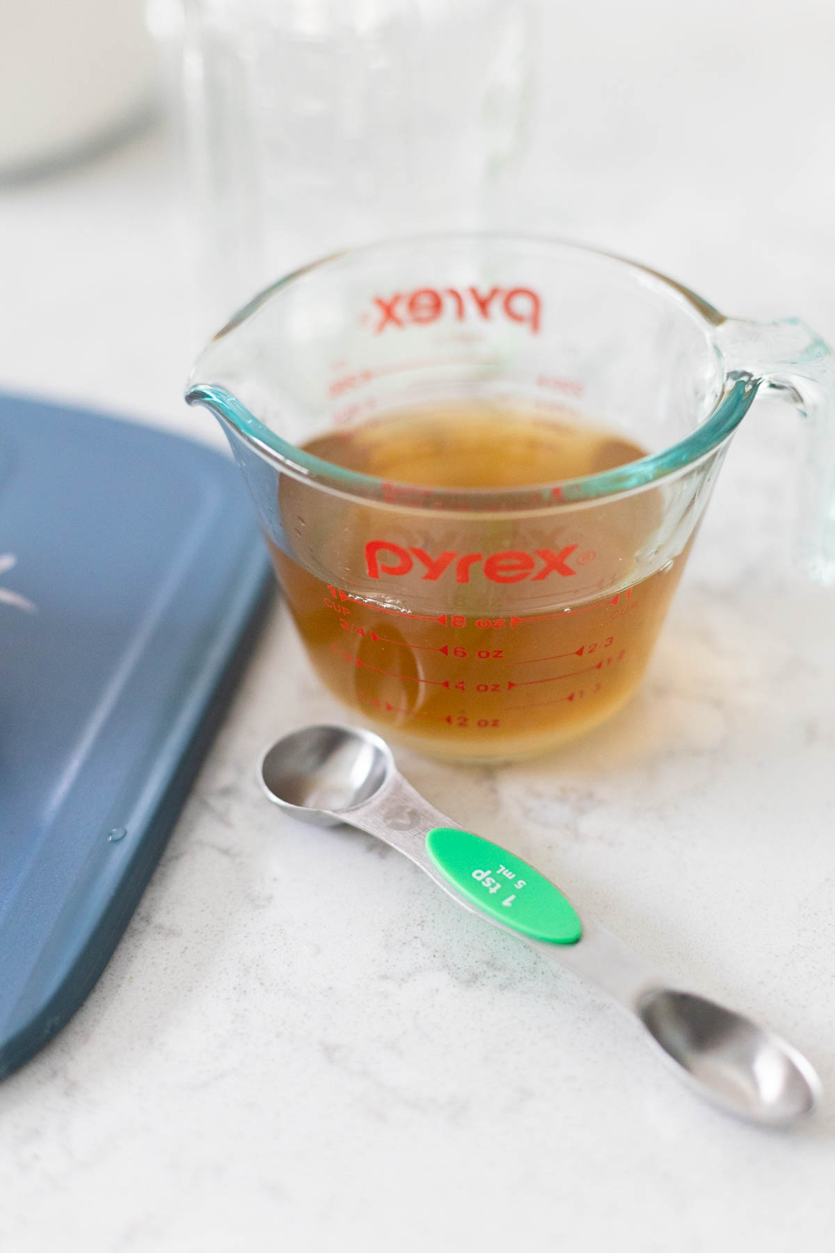 A measuring cup of vinegar has a measuring spoon on the side.