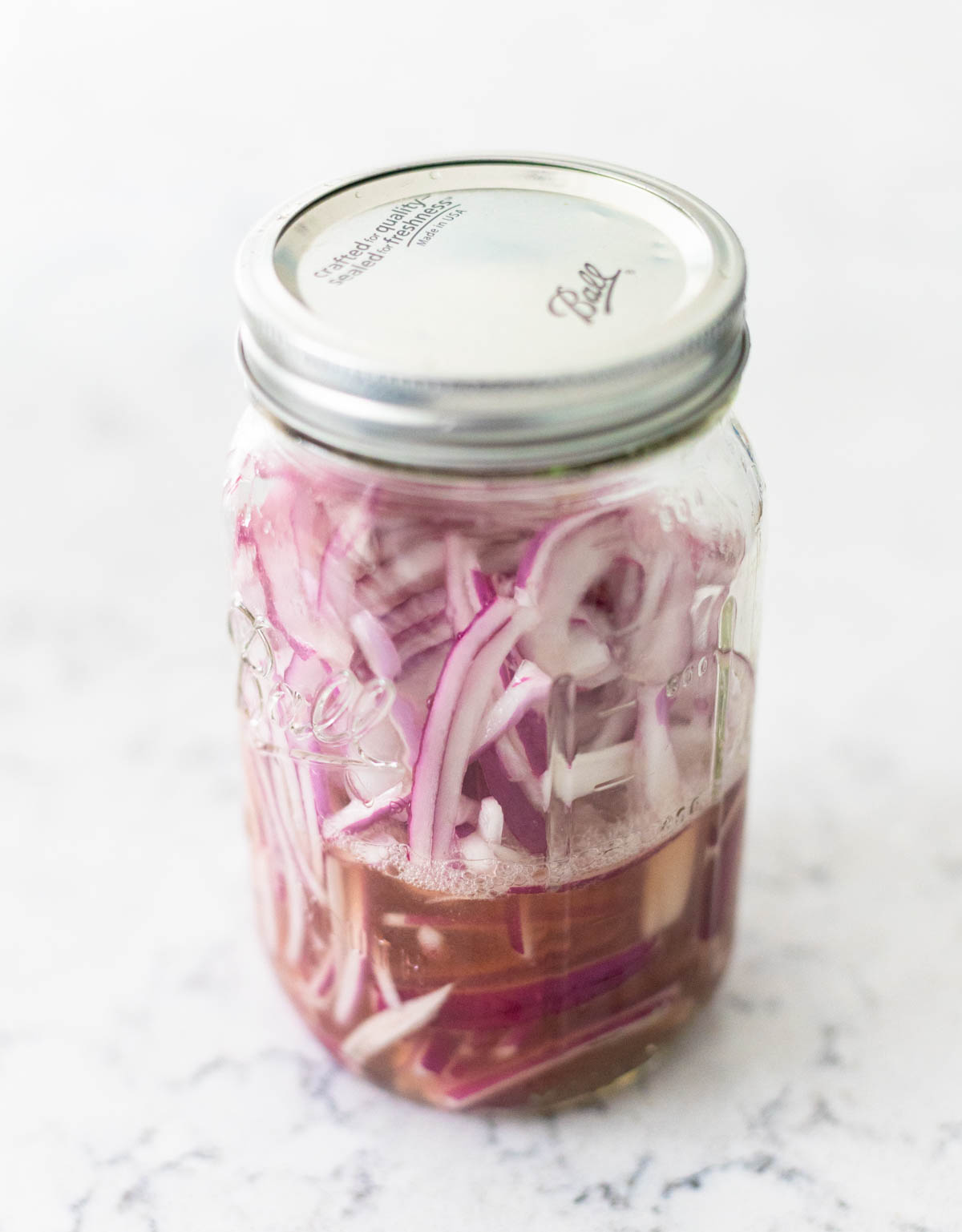 The sliced red onions are in a large mason jar.