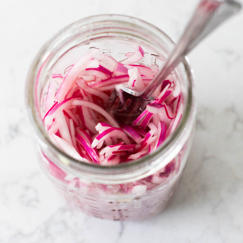 The finished red onions are in a mason jar being stirred with a fork.