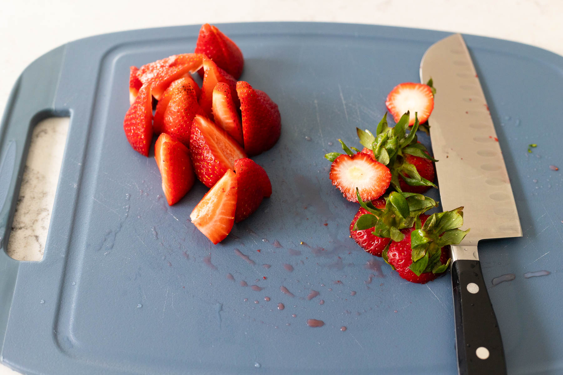 Fresh strawberries have been cut into quarters on a cutting board.