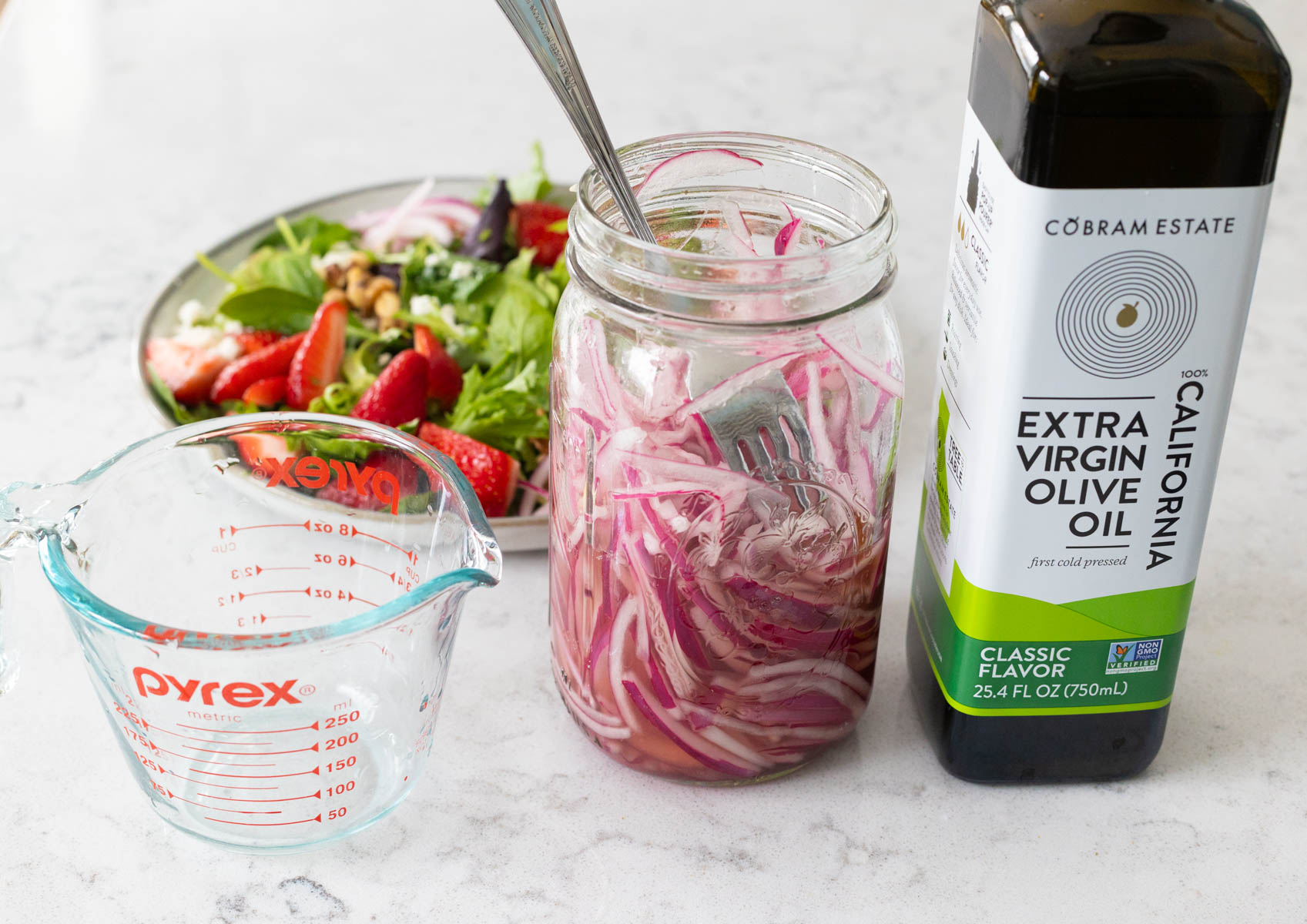 The jar of pickled red onions and olive oil are on the counter by the salad.