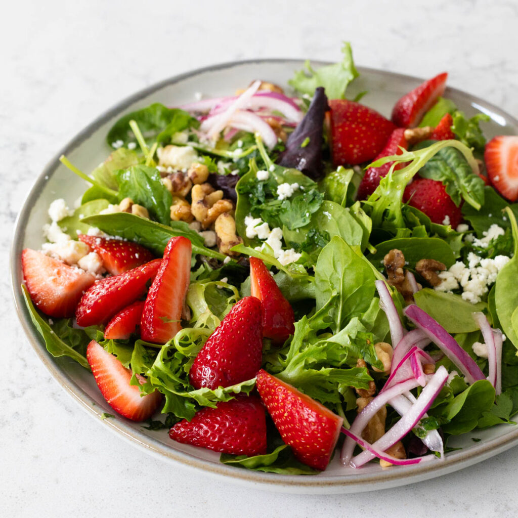 A plate filled with salad greens, fresh strawberries, and pickled red onions.