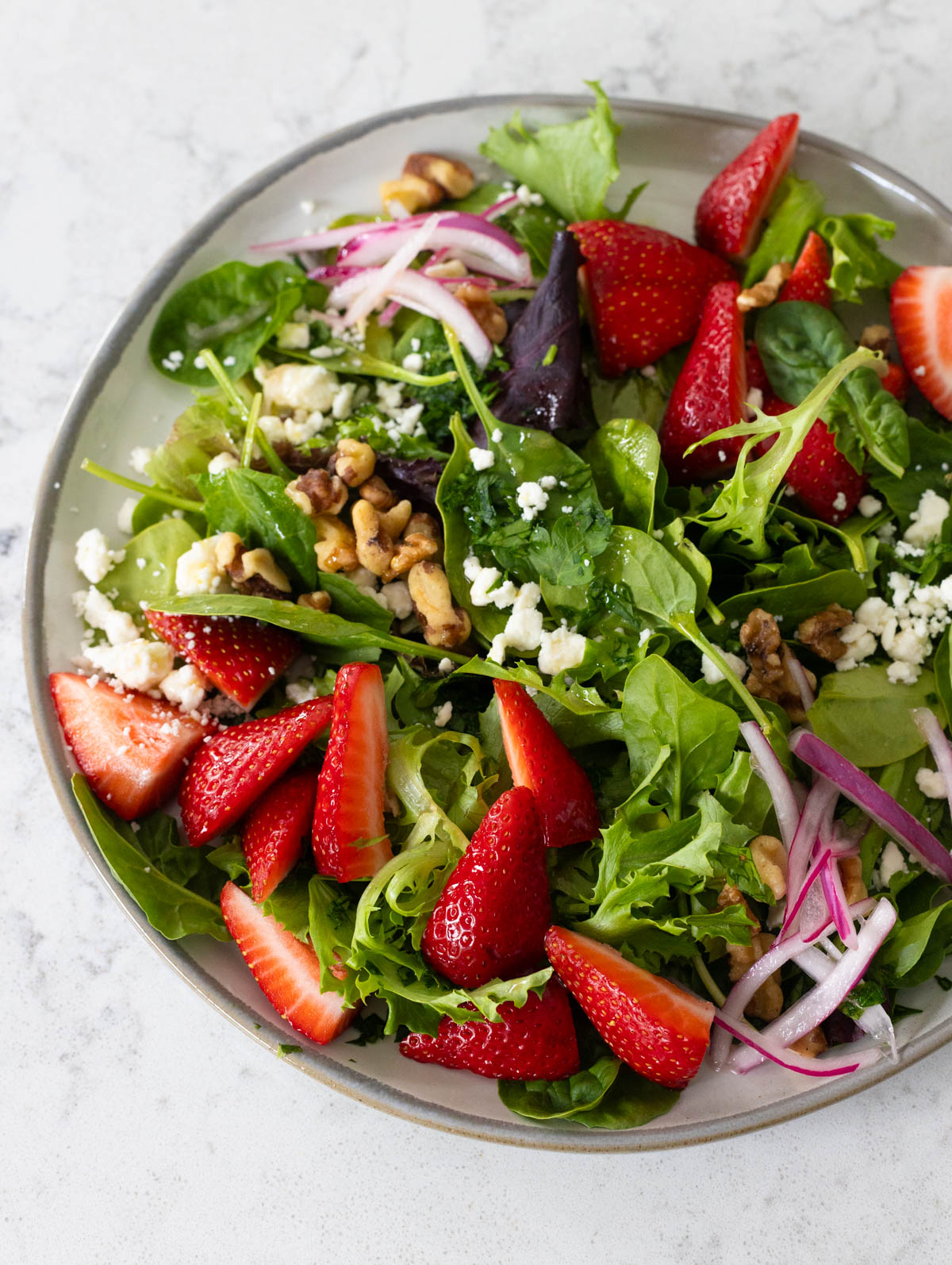 A plate filled with salad greens, fresh strawberries, and pickled red onions.