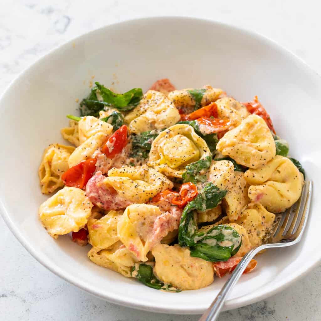 A bowl of tortellini is coated in a creamy boursin cheese sauce with tomatoes and spinach.