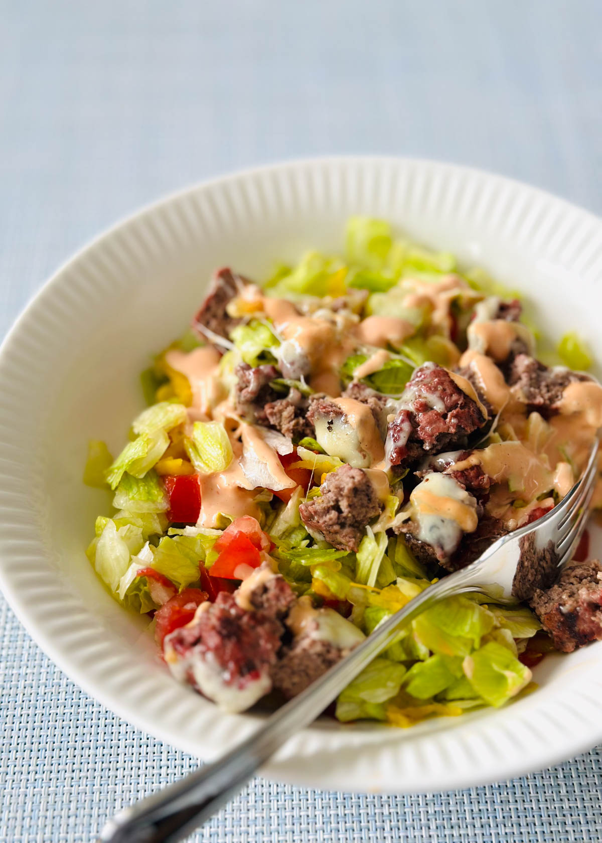 A white bowl filled with lettuce and topped with a chopped up cheeseburger.