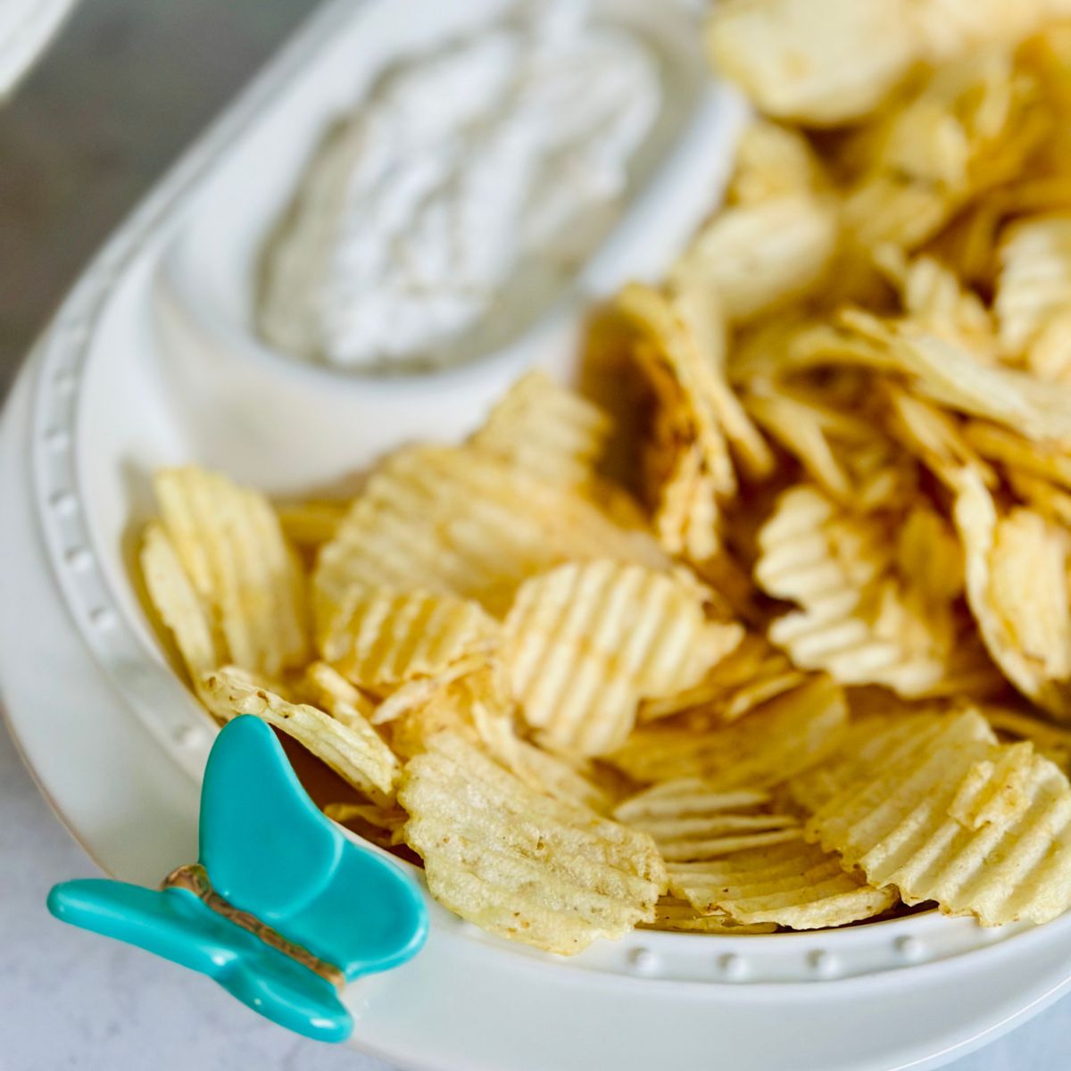 A bowl of potato chips with a creamy dip on the side.