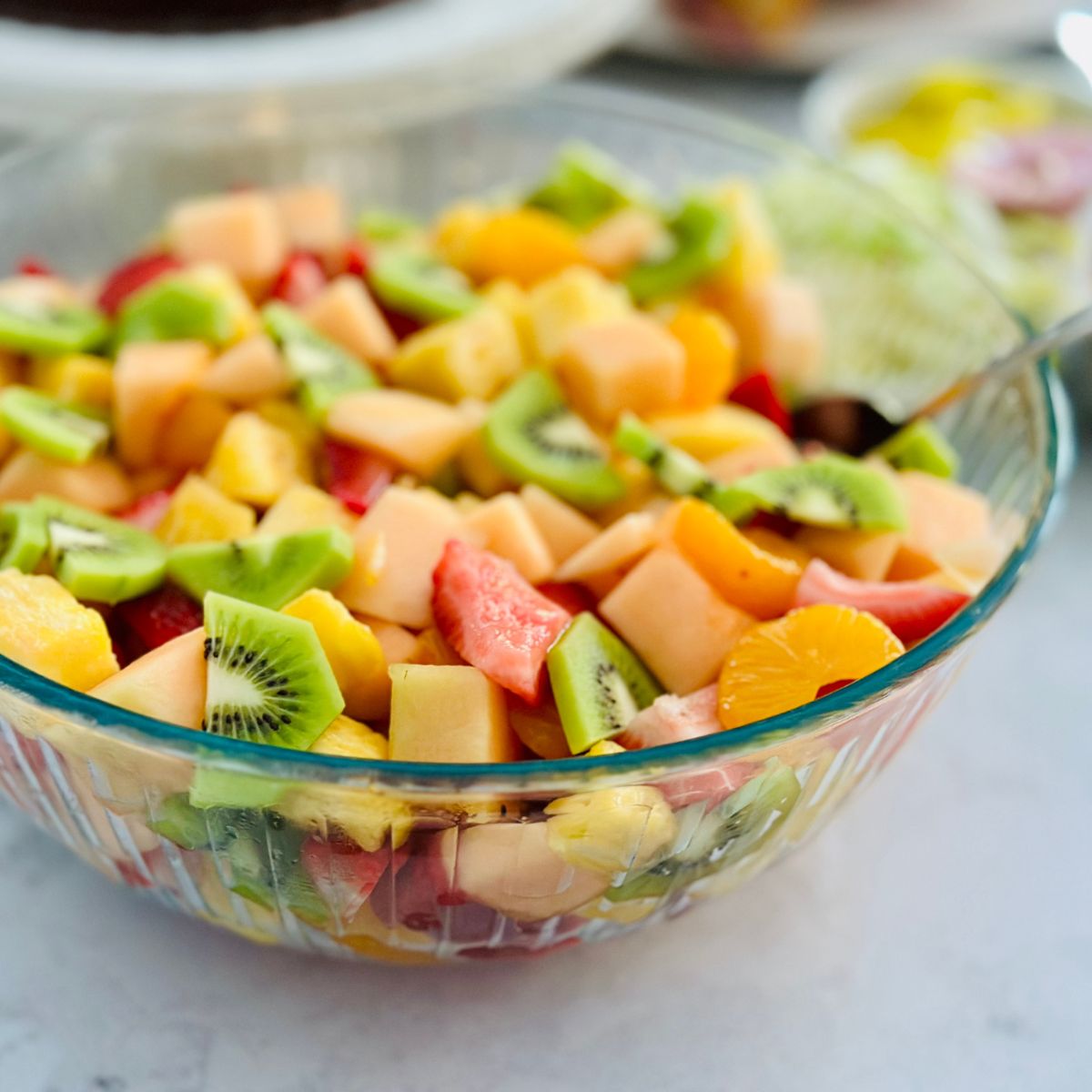 A big bowl of fruit salad has kiwi, cantaloupe, and strawberries.