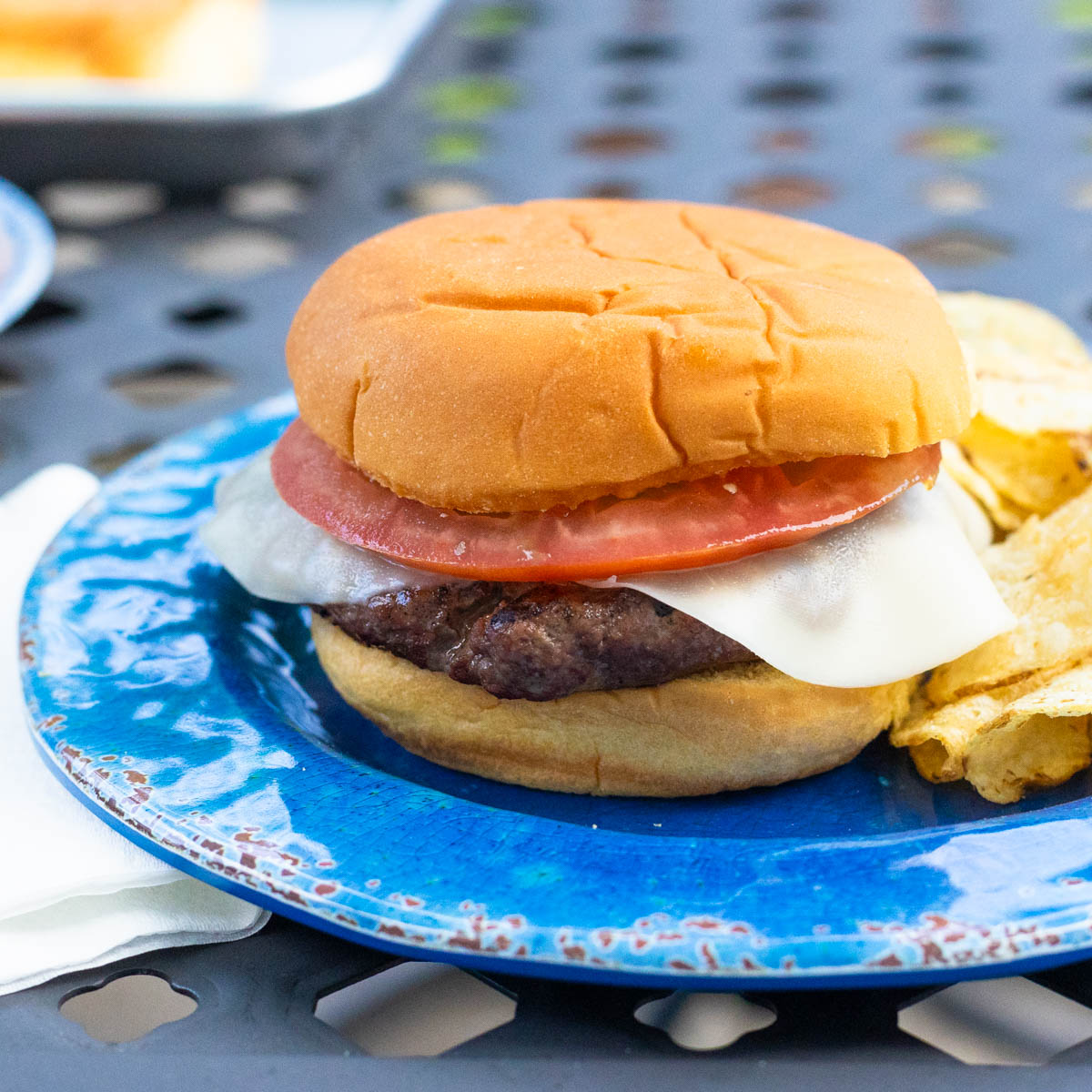 A simple hamburger with provolone cheese and a sliced tomato on a blue plate.