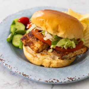 A seasoned fish filet is on a hamburger bun with shredded lettuce and a sliced tomato.