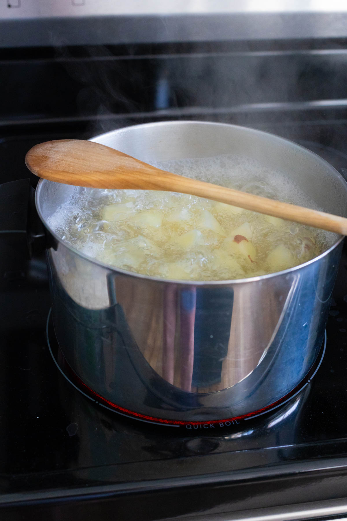 The potatoes are in a large pot of boiling water with a wooden spoon over the top.