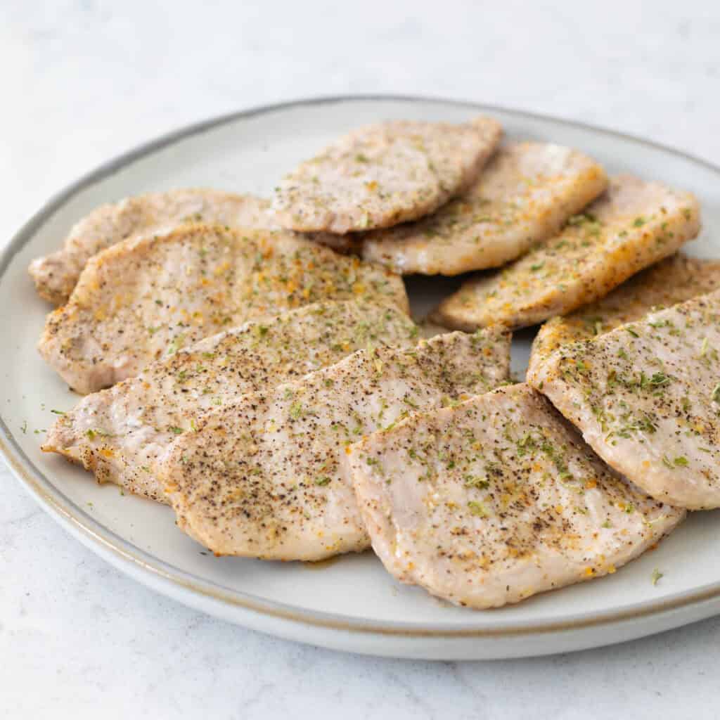 A plate has 10 thin cut pork chops seasoned and arranged for serving at dinner.