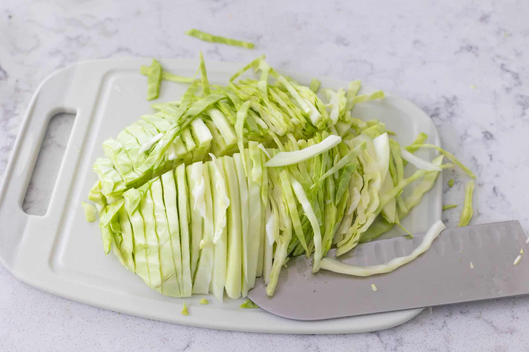 The cabbage head has been shredded on a cutting board.