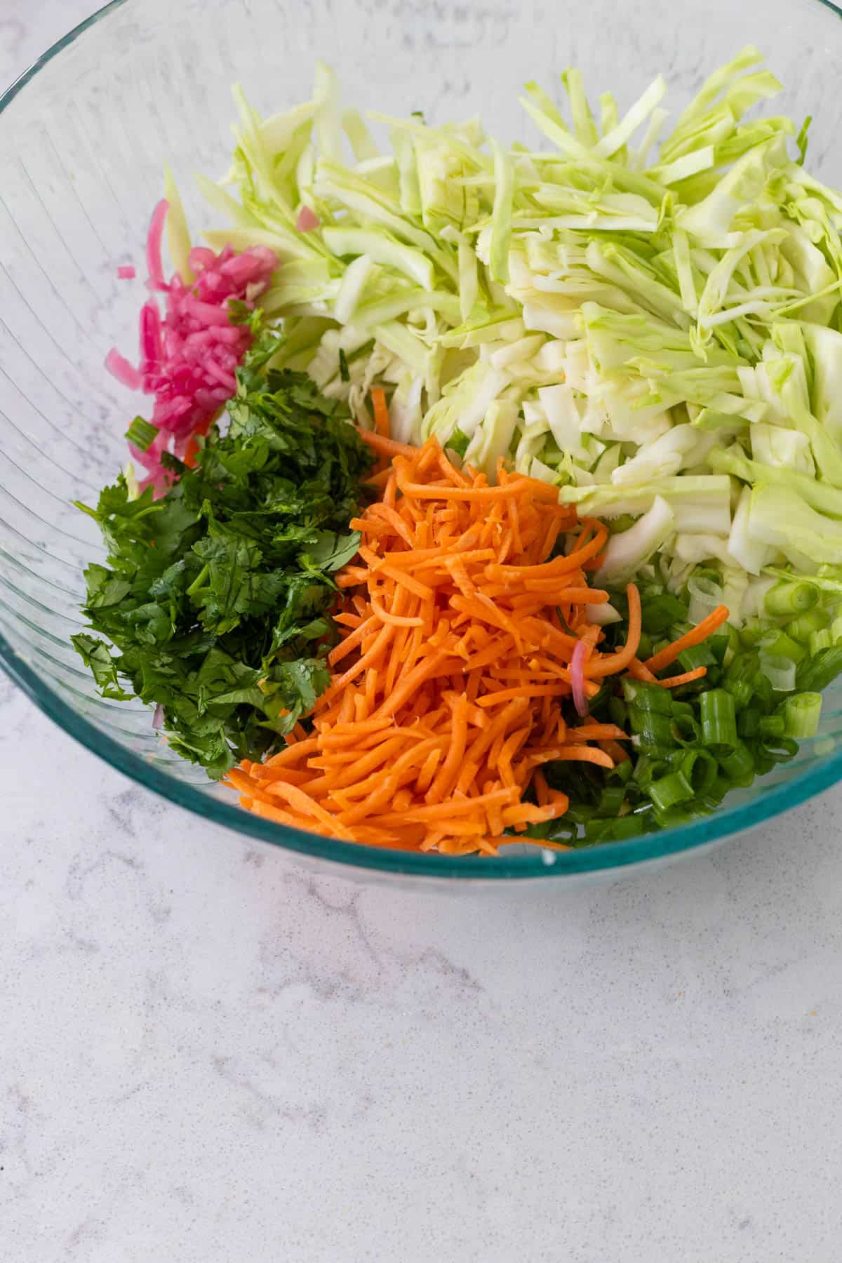 The mixing bowl is filled with shredded cabbage, shredded carrot, minced pickled onion, green onions, and chopped cilantro.