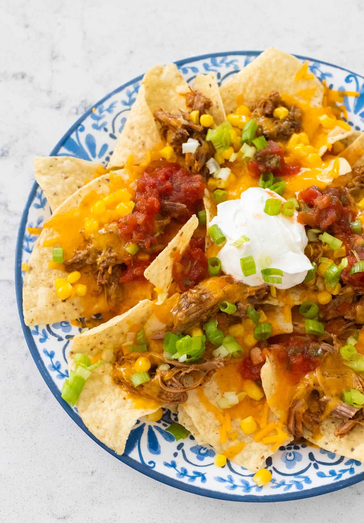 The plate of nachos has green onions, sour cream, and salsa on the top.