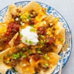 A plate of nachos has sour cream and salsa on the top.