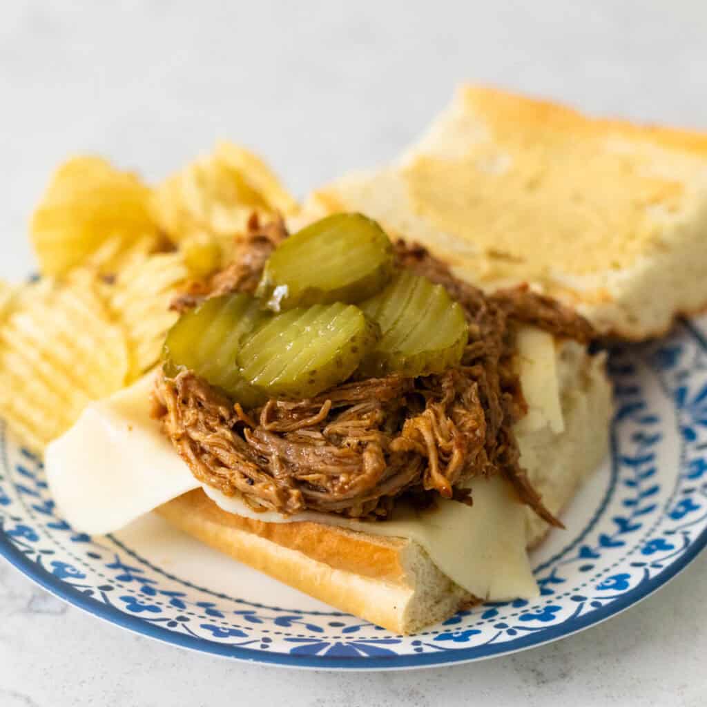 An open face Cuban pork sandwich shows the pile of pulled pork and pickles inside.