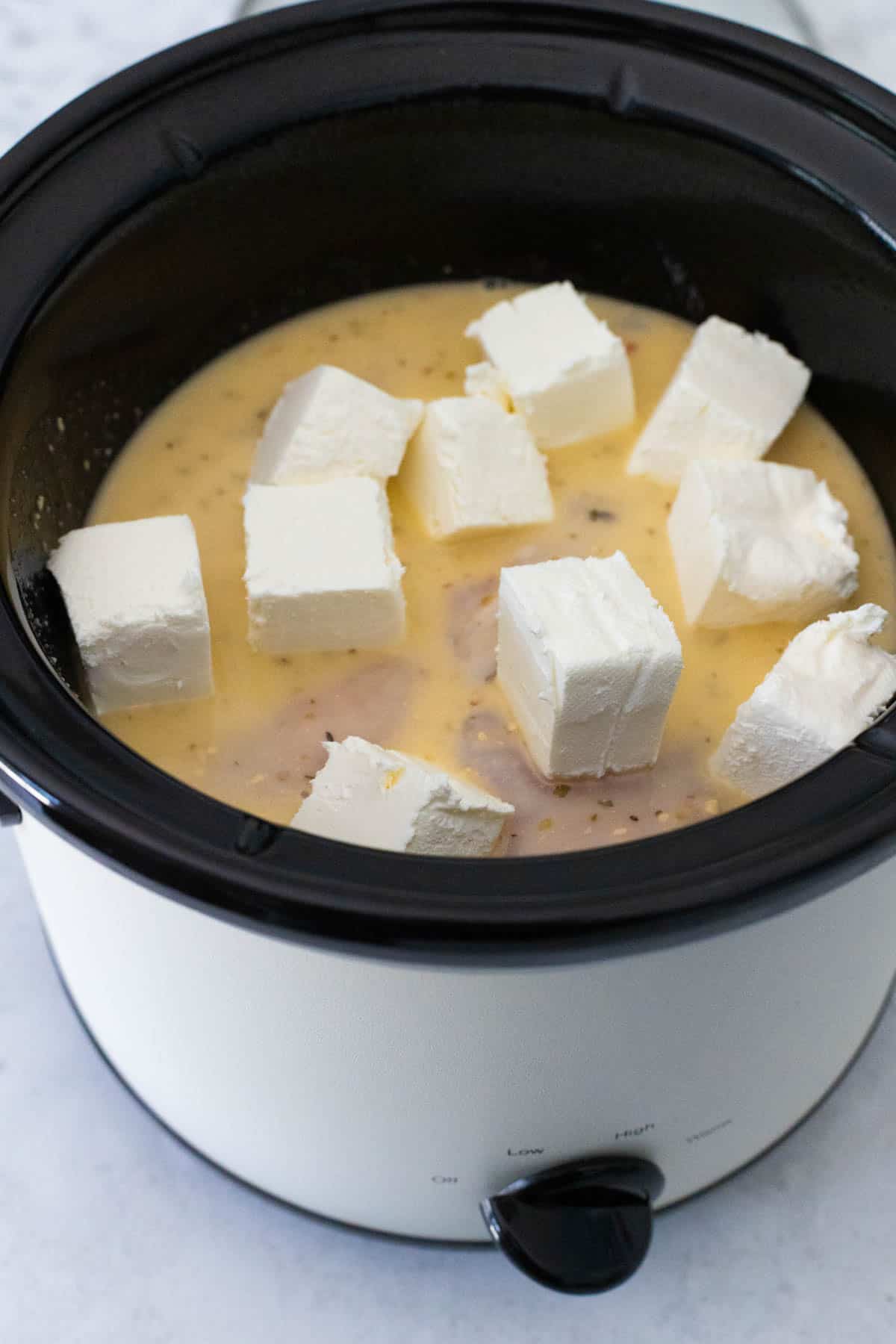 The cream cheese has been cut into cubes and put on top of the chicken.