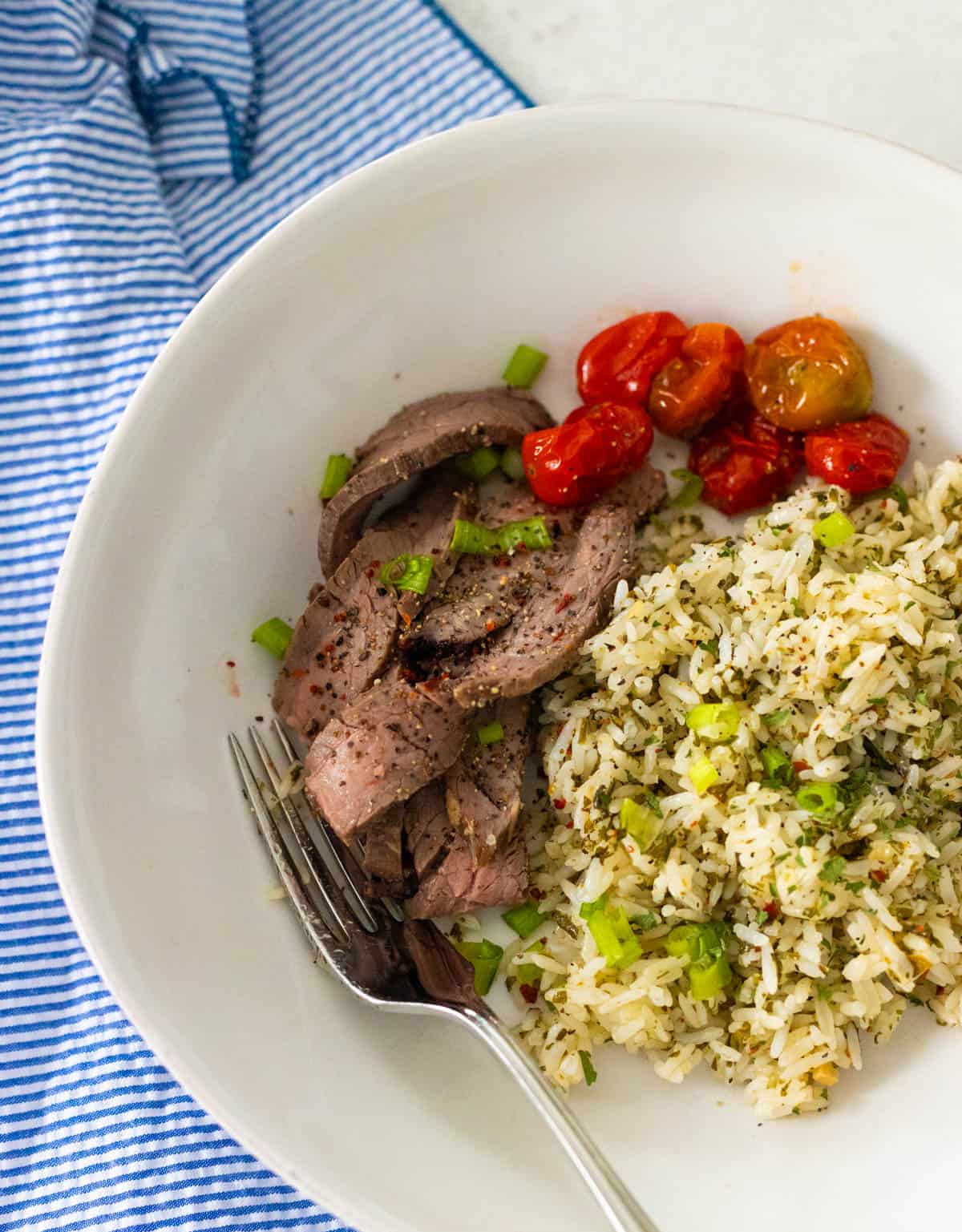 A flank steak has been thinly sliced and is served alongside cilantro chimichurri sauce with roasted tomatoes.