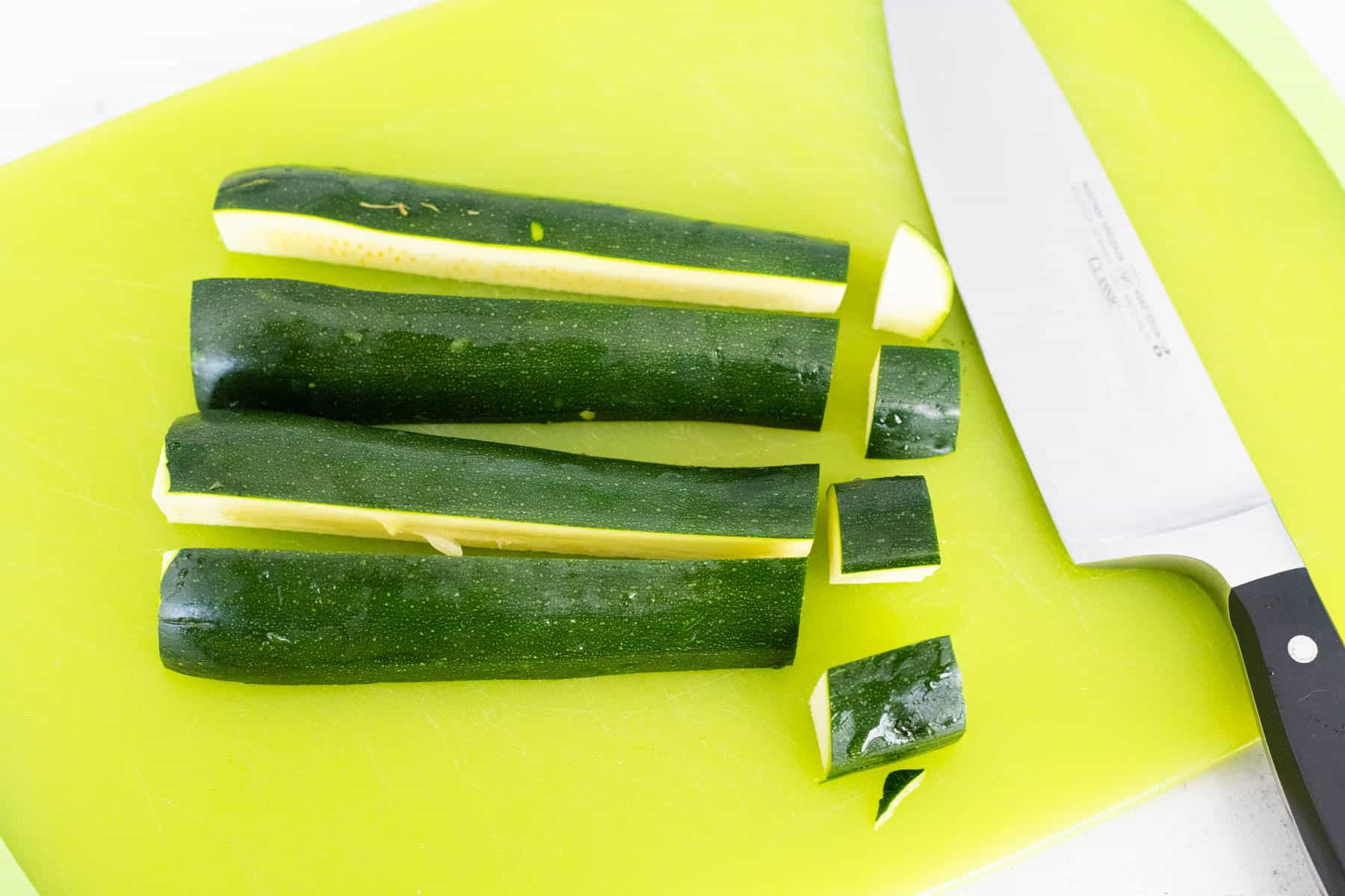 The zucchini have been sliced into four long strips and then cubed.