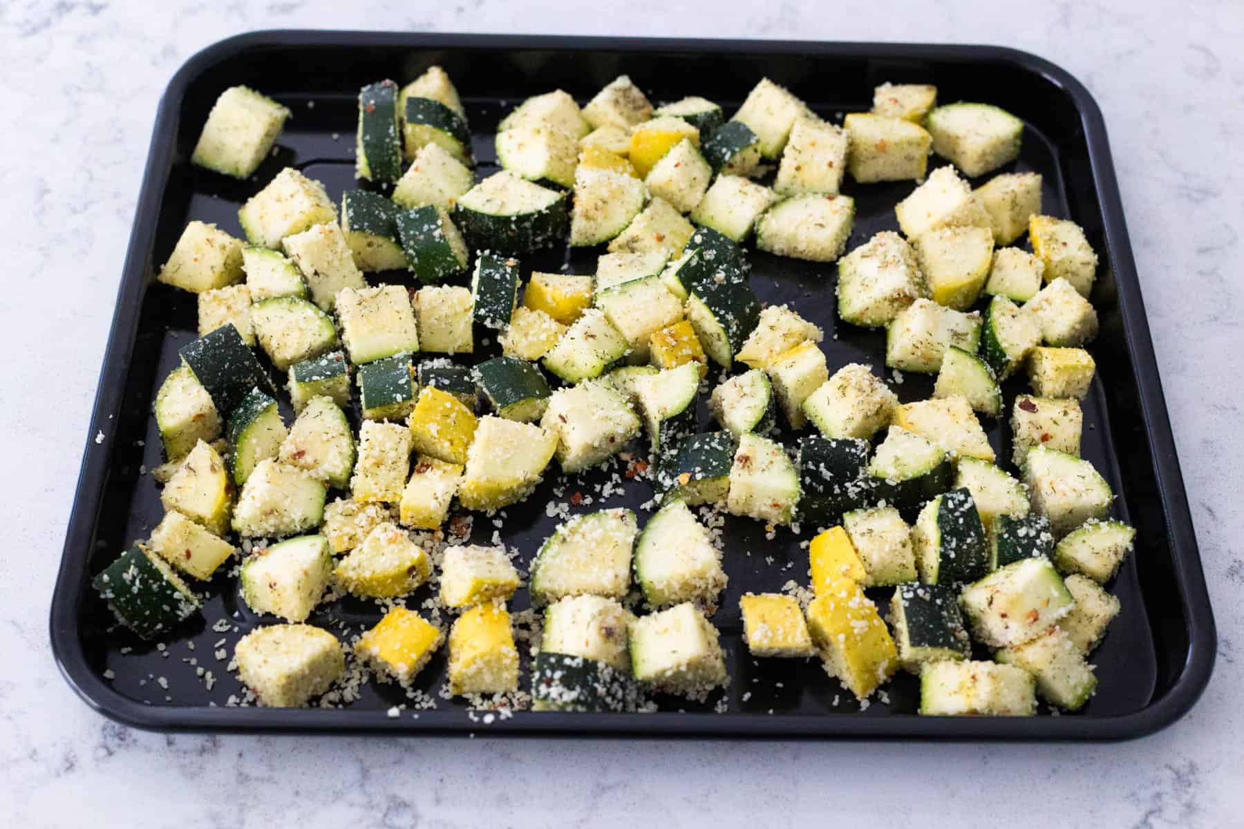 The prepared vegetables are spread into an even layer on a black baking sheet.