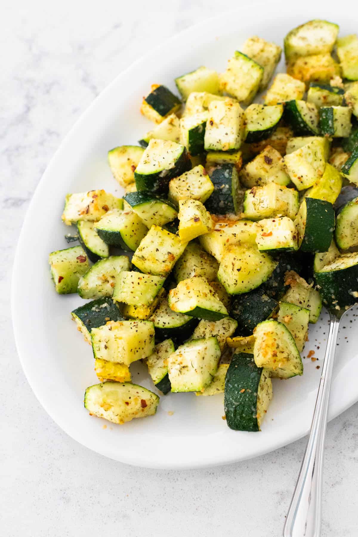 The white platter is filled with cubed zucchini roasted with parmesan over the top.