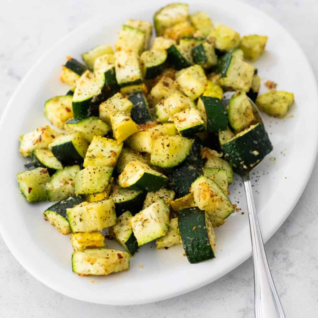 The white platter is filled with cubed zucchini roasted with parmesan over the top.