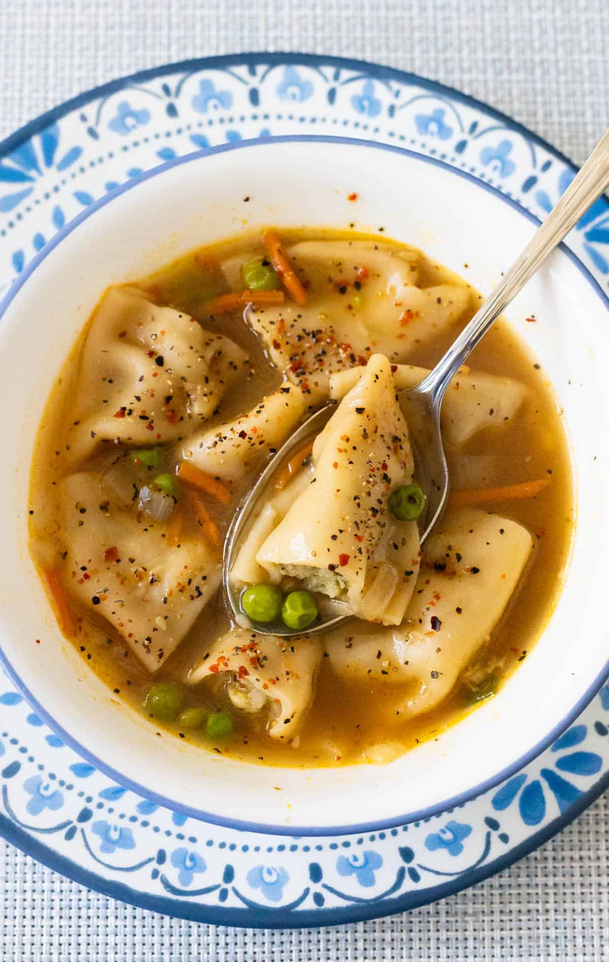 The white bowl is filled with potsticker soup. Half a dumpling is resting on the spoon to show the filling and the peas.