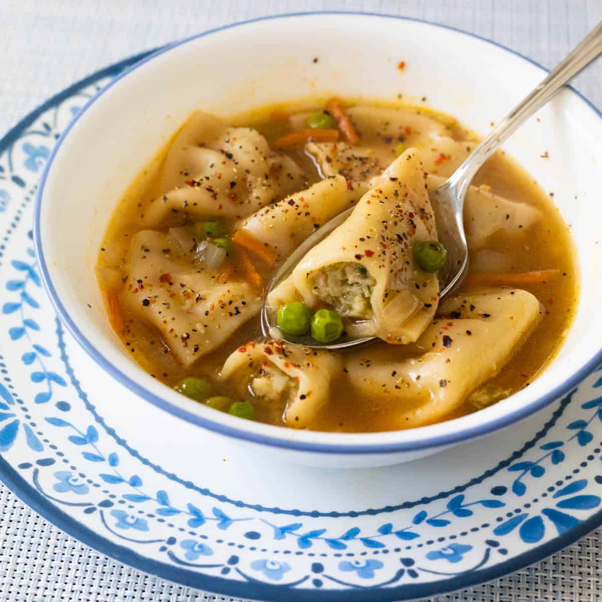 The white bowl is filled with potsticker soup. Half a dumpling is resting on the spoon to show the filling and the peas.