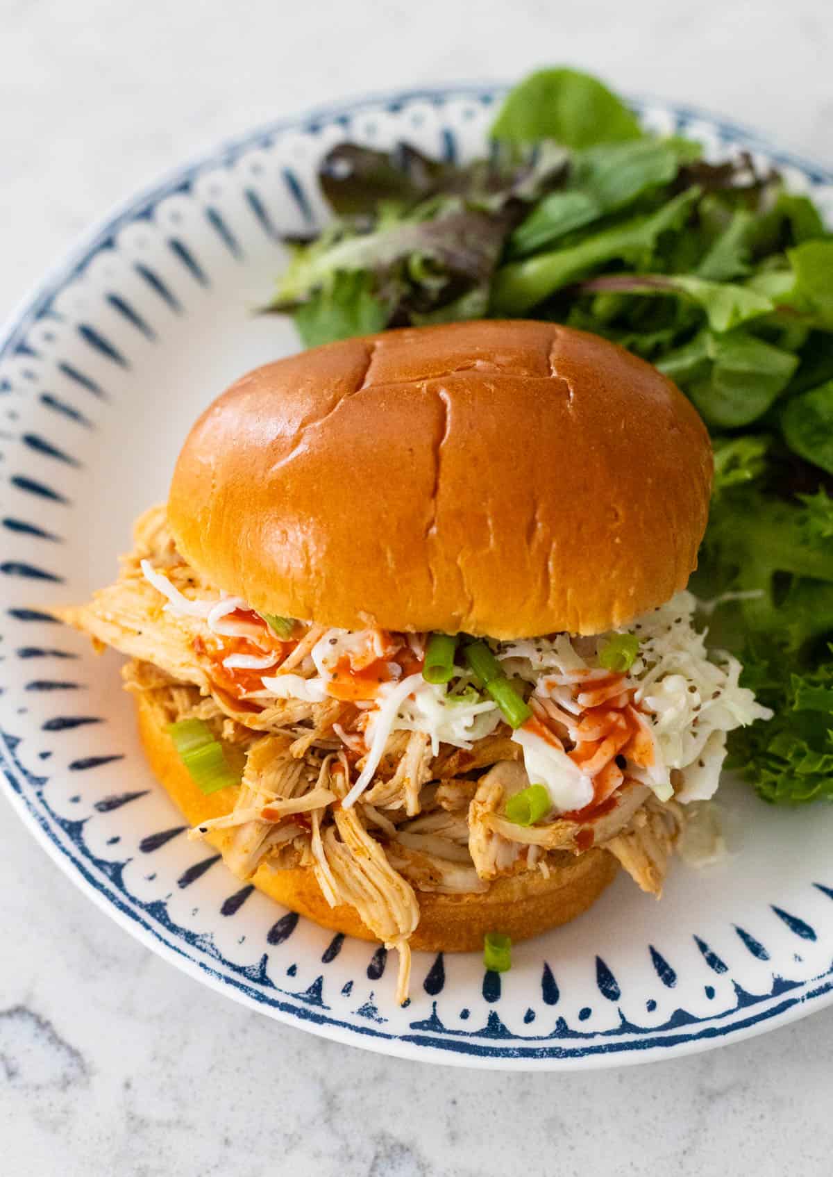 The shredded chicken is on a brioche bun with coleslaw. Hot sauce is drizzling down the sides.