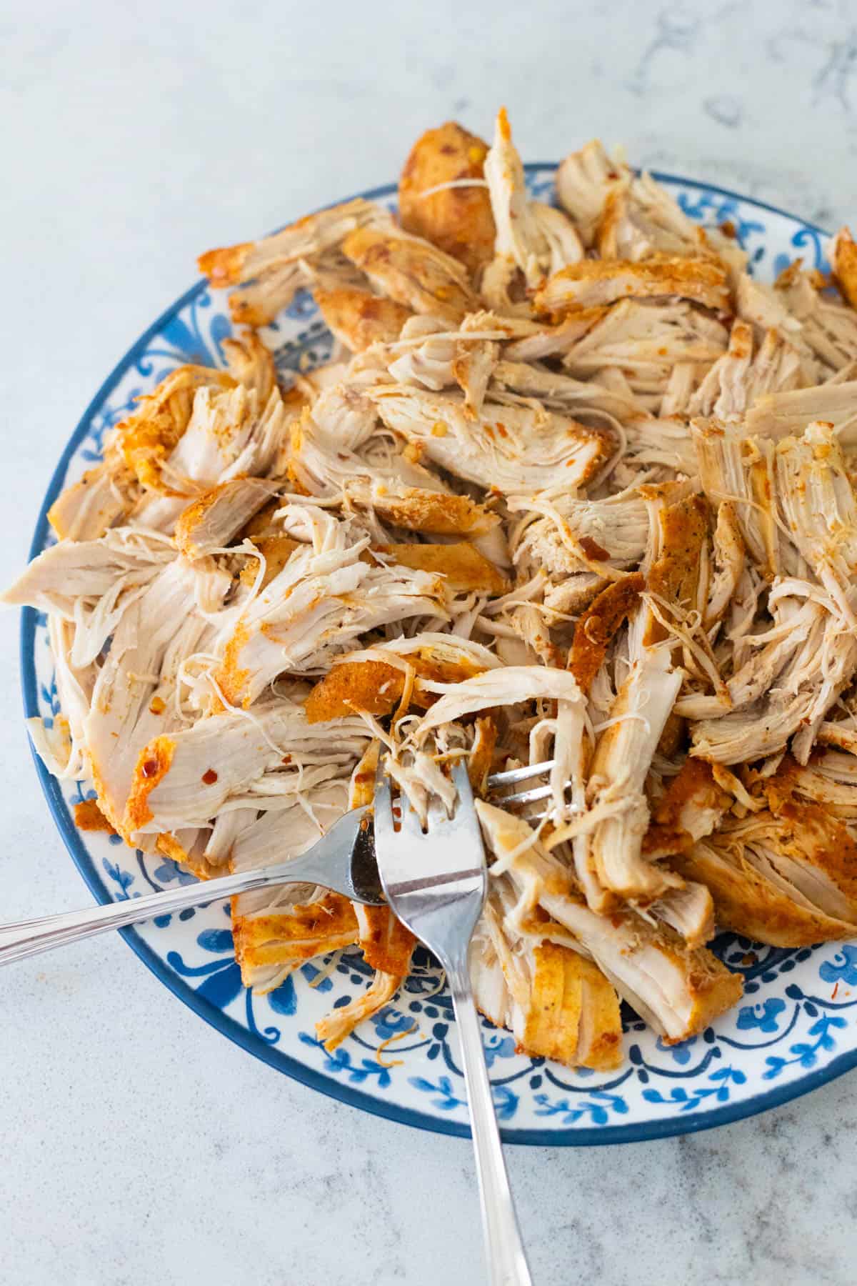 The chicken has been shredded with two forks on a dinner plate.